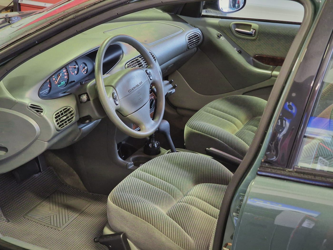 Wnętrze Chryslera Cirrus z 1995 roku: szałwiowozielone welurowe fotele, kierownica z logo Chryslera i deska rozdzielcza