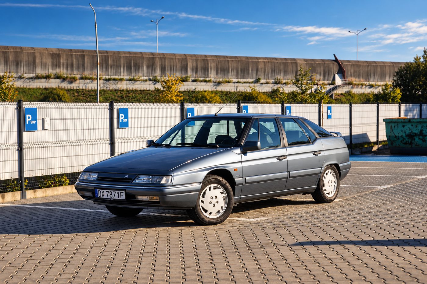 Srebrny Citroën XM w ciepłym świetle zachodzącego słońca, widok z przodu i z boku na parkingu