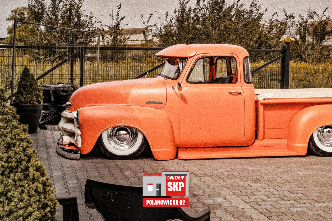 Pomarańczowy Chevrolet 3100 pickup na obniżonym zawieszeniu, na kostce przed stacją SSCAR